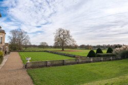 A large, manicured lawn with trimmed hedges and trees sets the perfect scene, bordered by a stone walkway and fence—ideal for capturing timeless moments as a Hartham Park wedding photographer.