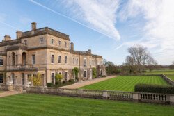 A grand historic mansion with a stone facade and manicured lawns under a clear blue sky, perfect for capturing unforgettable moments as your Hartham Park wedding photographer.