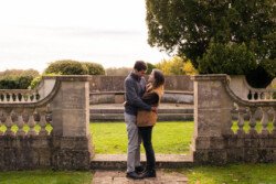 A couple embraces in a garden setting with stone railings and green grass, captured beautifully by a Hartham Park wedding photographer.