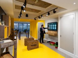 OLYMPUS DIGITAL CAMERA A person in a suit points to a presentation on a screen in a modern office with yellow accents and wooden decor, exemplifying the polished professionalism captured by our Corporate Photography & Video Services.