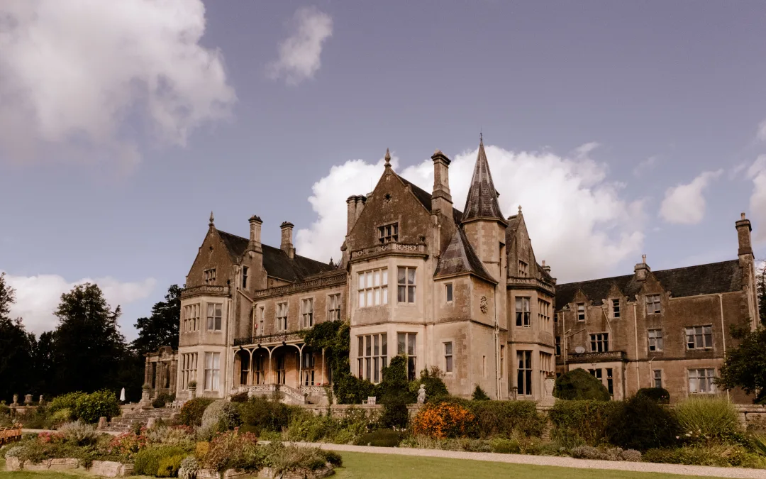A large mansion sitting on a lush green lawn. Orchardleigh House Weddings