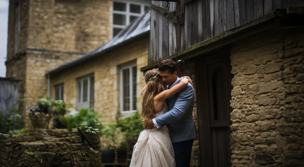 A bride and groom hugging in front of a stone building. Longhouse Wedding Photographer and at The Gathering Barn