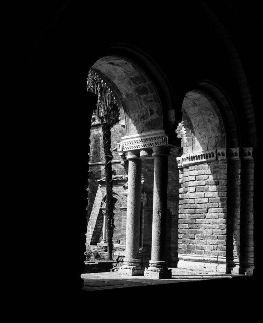 Black & White Film Photography captures old stone arches and columns, partially in shadow, with sunlight illuminating the brickwork outside.